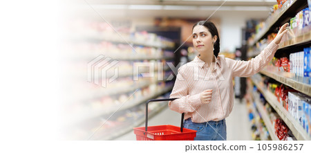 Web banner of shopping in supermarket. Portrait of young attractive caucasian woman takes food from shelve. Copy space. Concept of consumerism Web banner of shopping in supermarket. Portrait of young attractive caucasian woman takes food from shelve. Copy space. Concept of consumerism 105986257