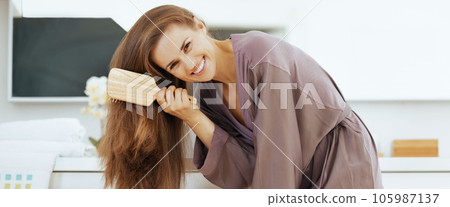 Happy young woman combing hair in bathroom Happy young woman combing hair in bathroom 105987137