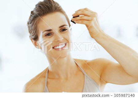Young woman applying cosmetic serum in bathroom 105987140