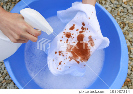 A woman is trying to wash off a stain on white clothes. A woman is trying to wash off a stain on white clothes. 105987214