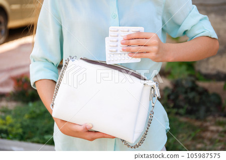 A woman puts pills in a white purse. A woman puts pills in a white purse. 105987575