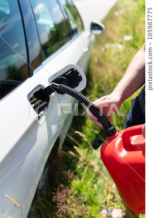 The driver fills up the empty tank of the car from a red canister on the side of the road. Close-up, vertical photo. 105987775