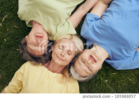 Top view of smiling mature women friends lying head to head on grass and with closed eyes 105988057