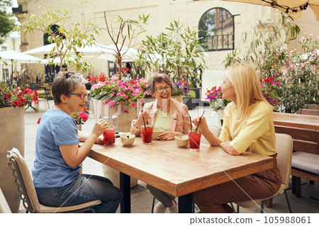 Mature female friends sitting in cafe, drinking cocktails and laughing while enjoying a lunch date Mature female friends sitting in cafe, drinking cocktails and laughing while enjoying a lunch date 105988061