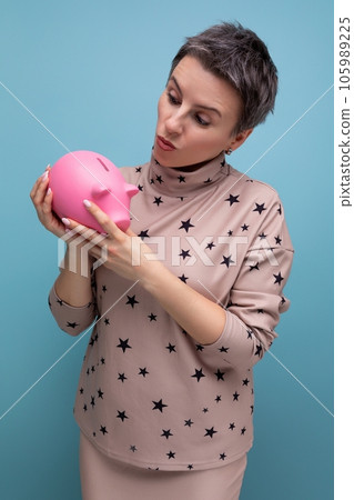 rich caucasian young business woman with a short haircut dressed in a beige suit holds a piggy bank 105989225