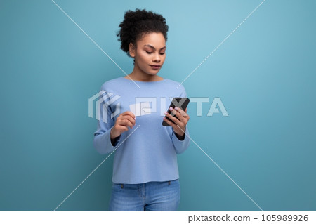 young brunette woman with afro hair pays for purchases using a card and smartphone 105989926
