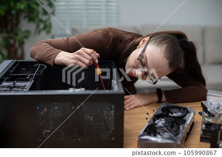 A young woman working in an office tries to fix a computer with a screwdriver. A young woman working in an office tries to fix a computer with a screwdriver. 105990867