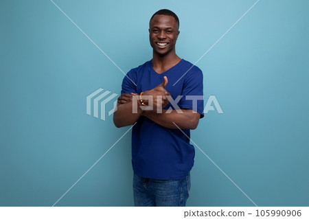 pleasant well-groomed cute young african man in a blue t-shirt on a blue background 105990906