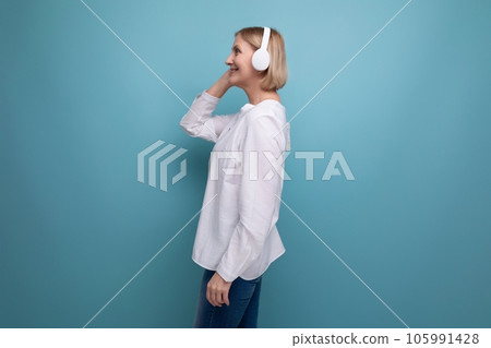 an adult woman with a blond hairdo dances to music in wireless headphones 105991428