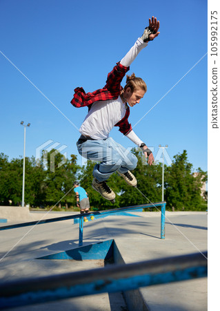 Young guy wearing rollerblades jumping from handrail on outdoor rollerdrome 105992175