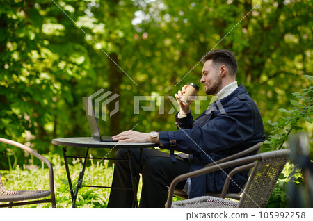 Businessman working on laptop drinking coffee at cafe in park 105992258