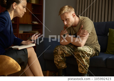 Military man hugging himself suffering from bad memories during therapy session 105992423
