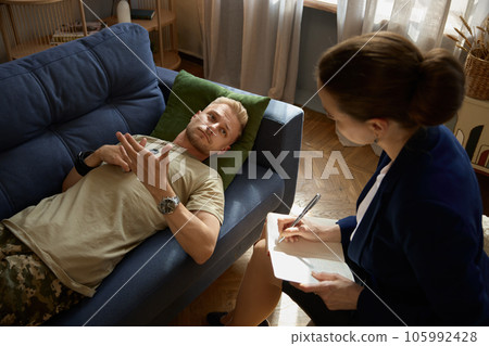 Frustrated sad soldier with ptsd talking at psychiatrist during therapy session 105992428