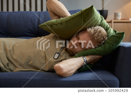 Stressed soldier man covering ears with pillow trying drown out voices in head 105992429