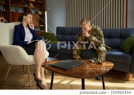 Worried soldier talking to doctor psychologist during therapy session 105992434