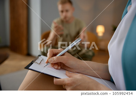 Distraught military veteran talks with counselor with focus on writing hand 105992454