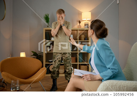 Woman psychologist calming nervous military man crying during therapy session 105992456