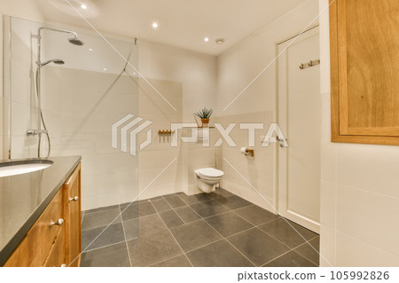 a modern bathroom with black tile flooring and wooden cabinetd cabinets in the corners on the left side 105992826