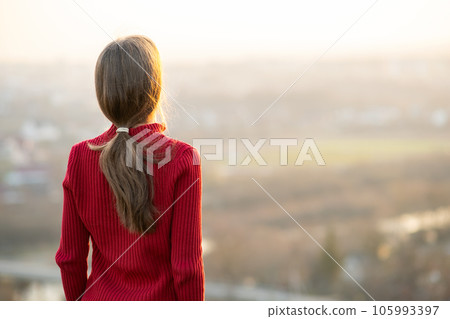 Young woman in red jacket standing outdoors enjoying evening view. Relaxing, freedom and wellness concept. 105993397