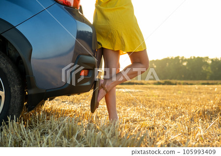 Young woman driver legs in yellow summer dress standing near her car enjoying warm summer day at sunset. Young woman driver legs in yellow summer dress standing near her car enjoying warm summer day at sunset. 105993409