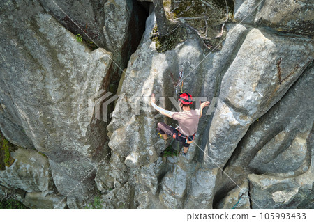Young man climbing steep wall of rocky mountain. Male climber overcomes challenging route. Engaging in extreme sport concept. Young man climbing steep wall of rocky mountain. Male climber overcomes challenging route. Engaging in extreme sport concept. 105993433