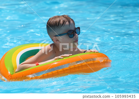 Young joyful child boy having fun swimming in inflatable air circle in swimming pool with blue water on warm summer day on tropical vacations. Summertime activities concept Young joyful child boy having fun swimming in inflatable air circle in swimming pool with blue water on warm summer day on tropical vacations. Summertime activities concept 105993435