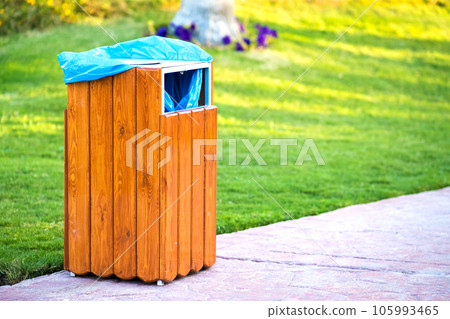 Yellow wooden trash can outdoors on the side of sidewalk in park. Garbage container on street outside . Yellow wooden trash can outdoors on the side of sidewalk in park. Garbage container on street outside . 105993465