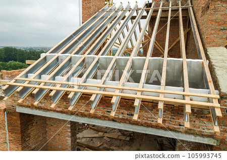 Unfinished brick apartment building with wooden roof structure under construction. 105993745