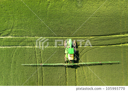 Tractor spraying chemical pesticides with sprayer on the large green agricultural field at spring 105993770