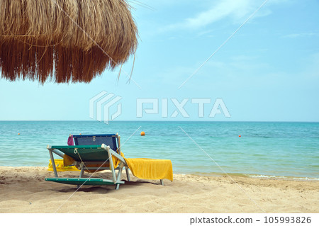 Straw shade umbrellas on sea tropical beach with resting sunbeds against blue vibrant sky in summer 105993826