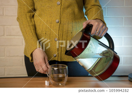 woman pouring hot water from a kettle into a clear glass mug 105994282