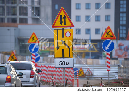 Roadworks warning traffic signs of construction work on city street and slowly moving cars Roadworks warning traffic signs of construction work on city street and slowly moving cars 105994327