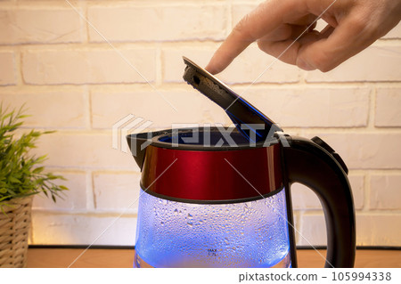 kettle with boiling water and a person 's finger closes the lid 105994338