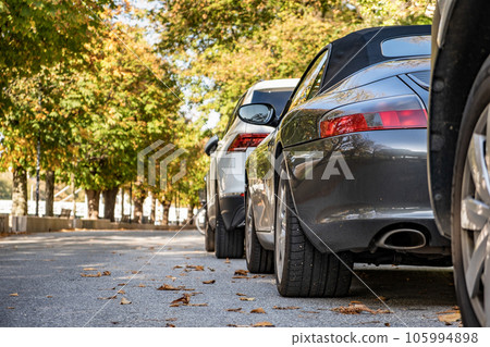 Modern cars parked on city street side in residential discrict. Shiny vehicles parked by the curb. Urban transportation infrastructure concept. Modern cars parked on city street side in residential discrict. Shiny vehicles parked by the curb. Urban transportation infrastructure concept. 105994898