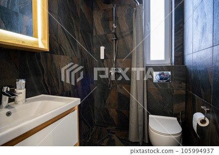 Interior of modern stylish bathroom with black tiled walls, curtain shower place and wooden furniture with wash basin and big illuminated mirror. Interior of modern stylish bathroom with black tiled walls, curtain shower place and wooden furniture with wash basin and big illuminated mirror. 105994937