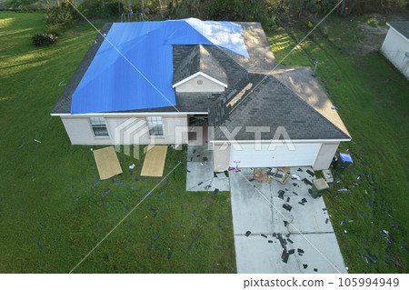 Hurricane Ian damaged house rooftop covered with protective plastic tarp against rain water leaking until replacement of asphalt shingles. Aftermath of natural disaster 105994949
