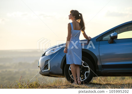 Happy woman driver in blue summer dress enjoying warm evening near her car. Travel and vacations concept. 105995202