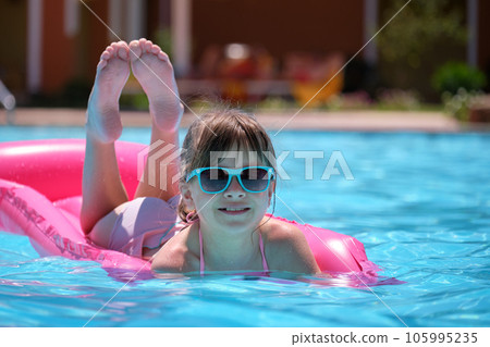 Happy child girl relaxing on inflatable air mattress in swimming pool on sunny summer day during tropical vacations. Summertime activities concept Happy child girl relaxing on inflatable air mattress in swimming pool on sunny summer day during tropical vacations. Summertime activities concept 105995235