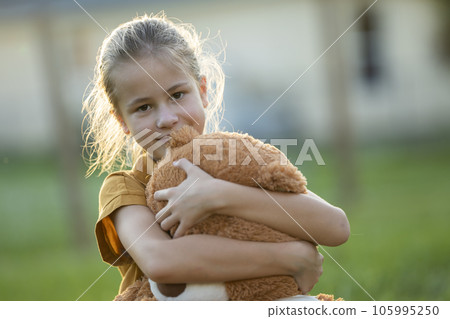 Happy child girl hugging her teddy bear friend outdoors on green grass lawn. Friendship concept 105995250