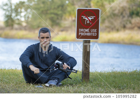 Drone operator is disappointed because he isn't allowed to fly his quadcopter in national park no drone area. Man is unable to use his UAV near restriction notice sign. Airspace use regulations Drone operator is disappointed because he isn't allowed to fly his quadcopter in national park no drone area. Man is unable to use his UAV near restriction notice sign. Airspace use regulations 105995282