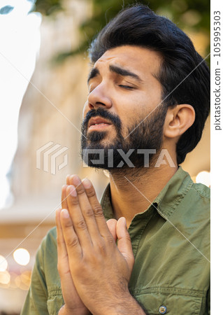 Portrait of indian man praying with closed eyes to God asking for blessing help forgiveness outdoors 105995303