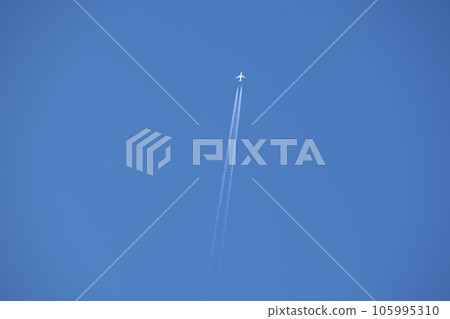 Distant passenger jet plane flying on high altitude on clear blue sky leaving white smoke trace of contrail behind. Air transportation concept. 105995310