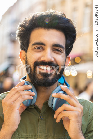 Happy young adult man in wireless headphones choosing, listening music dancing outdoors city street 105995343