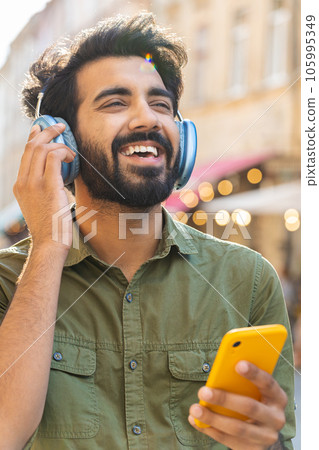 Happy young man in wireless headphones choosing, listening music dancing outdoors city street Happy young man in wireless headphones choosing, listening music dancing outdoors city street 105995349