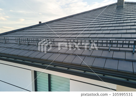 Closeup snow guard for safety in winter on house roof top covered with ceramic shingles. Tiled covering of building 105995531