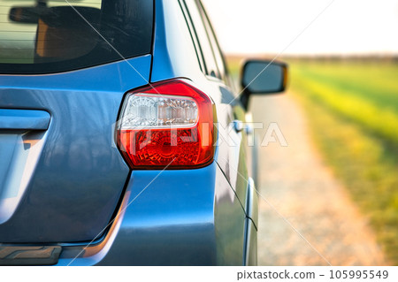Closeup of rear red taillight and mirror of new clean blue SUV off-road car on rural road 105995549