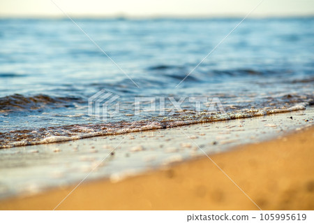 Close up of small sea waves with clear blue water over yellow sand beach at summer sunny shore. 105995619