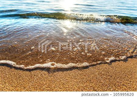 Close up of small sea waves with clear blue water over yellow sand beach at summer sunny shore. 105995620