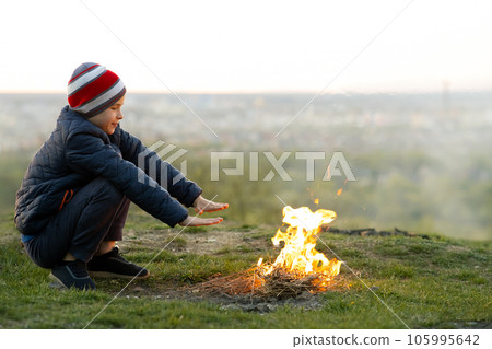 Child boy warming near bonfire outdoors in cold weather. 105995642