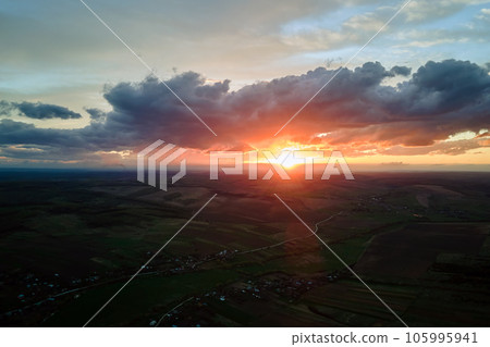 Bright colorful sunset sky with setting sun and vibrant clouds over dark landscape Bright colorful sunset sky with setting sun and vibrant clouds over dark landscape 105995941